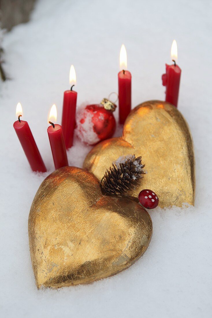 Goldene Herzen mit roten Kerzen im Schnee