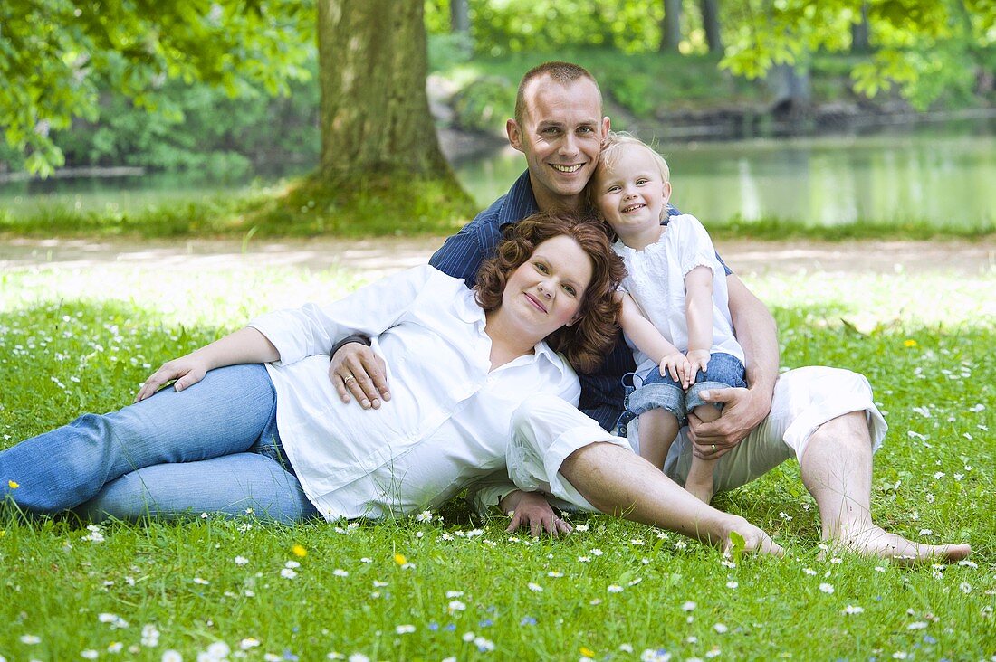 A happy young family lying on the grass by the lake