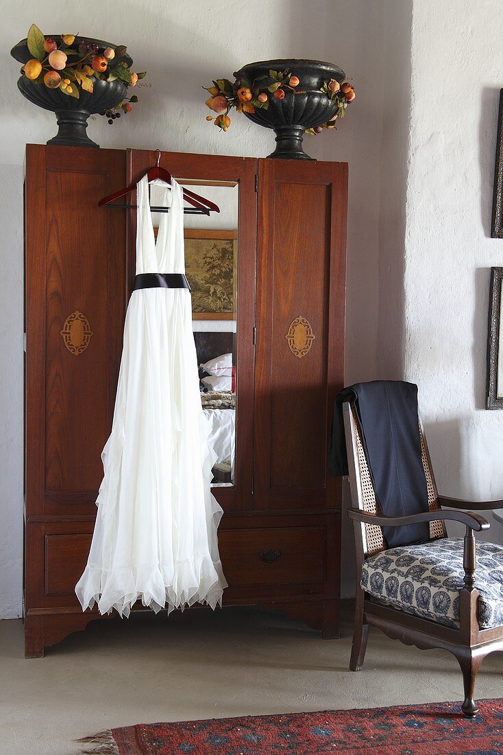 Elegantes weisses Kleid hängt an einem antiken Kleiderschrank
