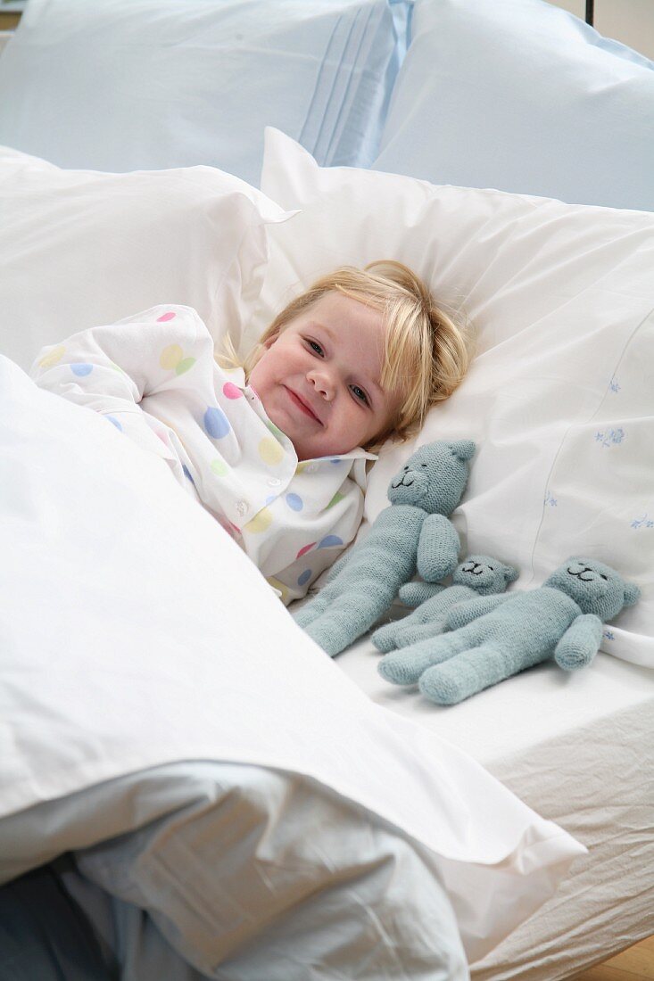 Kleines Mädchen liegt mit Kuscheltieren im Bett