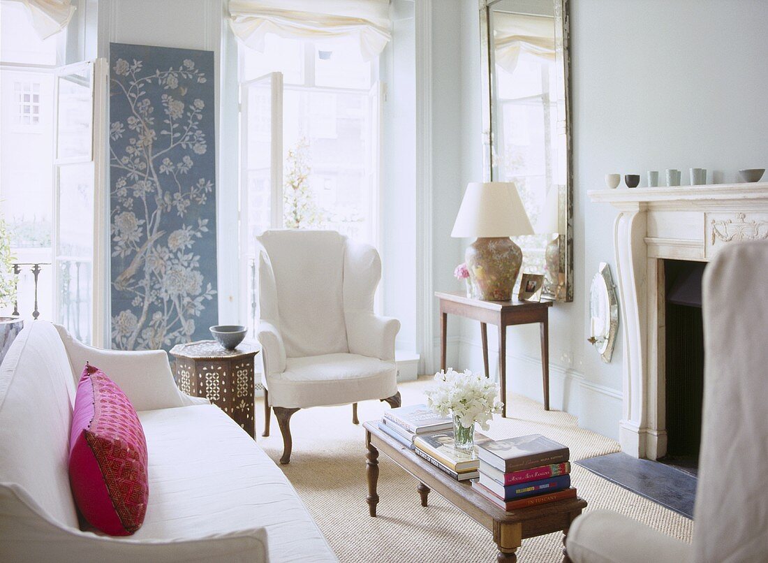 A traditional sitting room with fireplace, upholstered sofa and wing back armchair, French doors, wall hanging