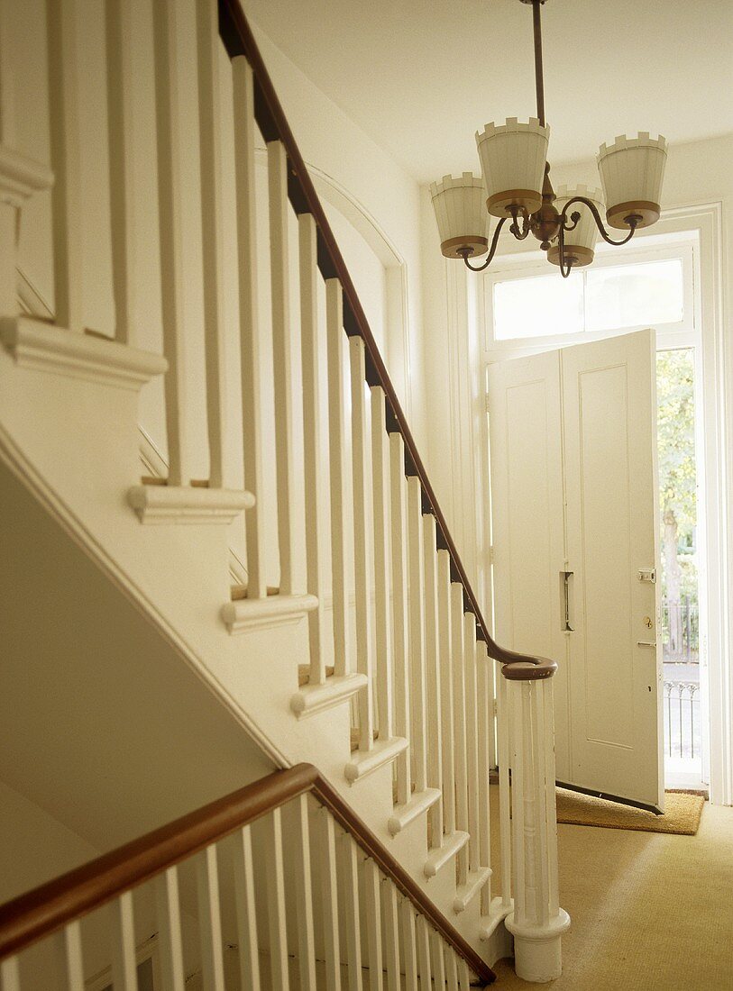 Staircase with wooden banister in white hallway with open door.