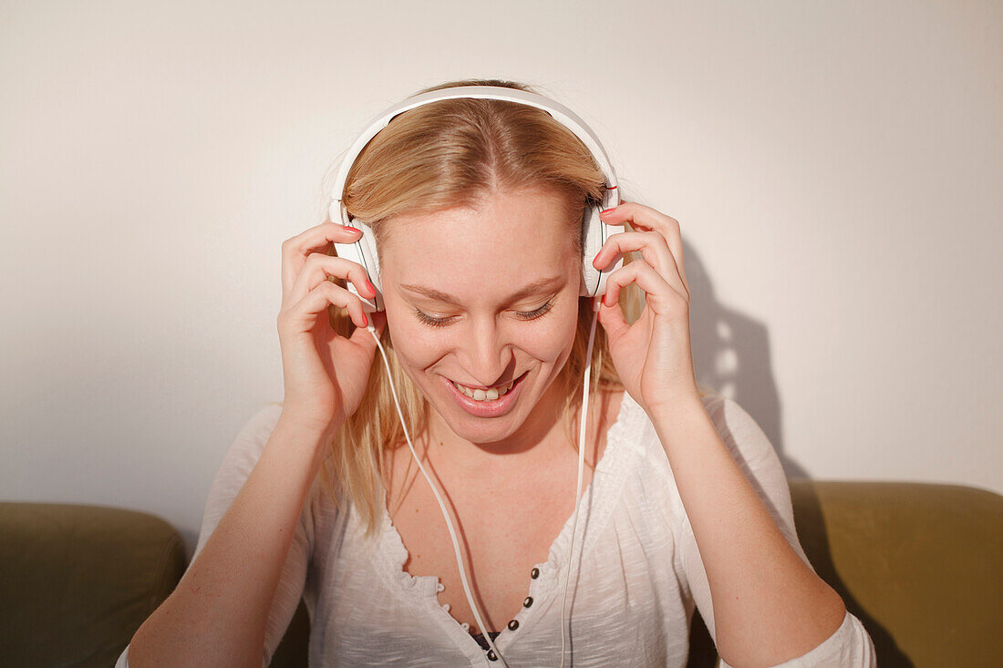 Young woman sitting on the sofa, listening to music