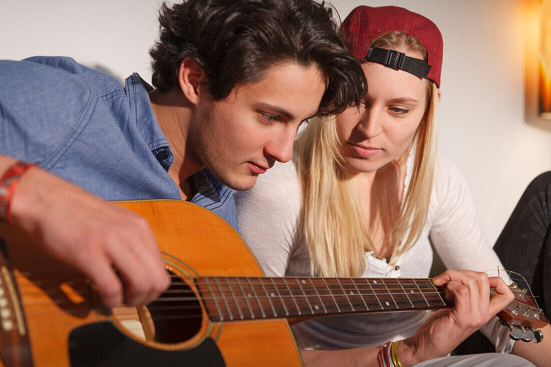 Junges Paar entspannt sich auf dem Sofa und spielt Gitarre