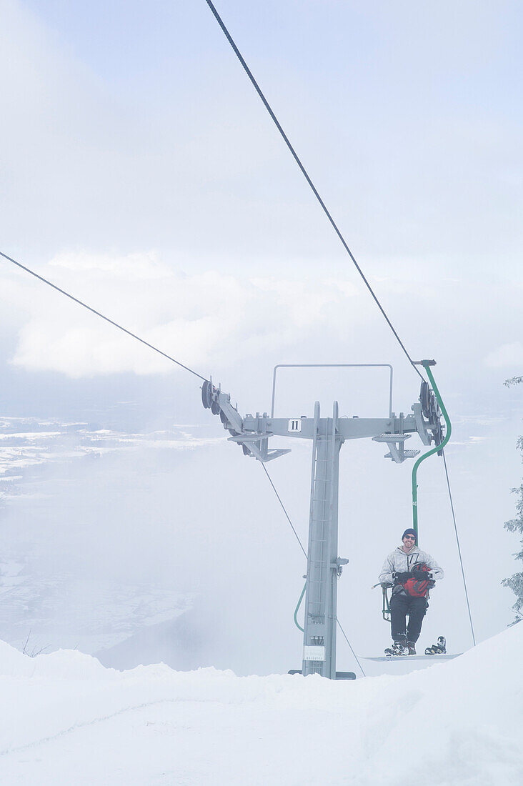 Snowboarder in a single chair lift, Kampenwand, Alps, Bavaria, Germany