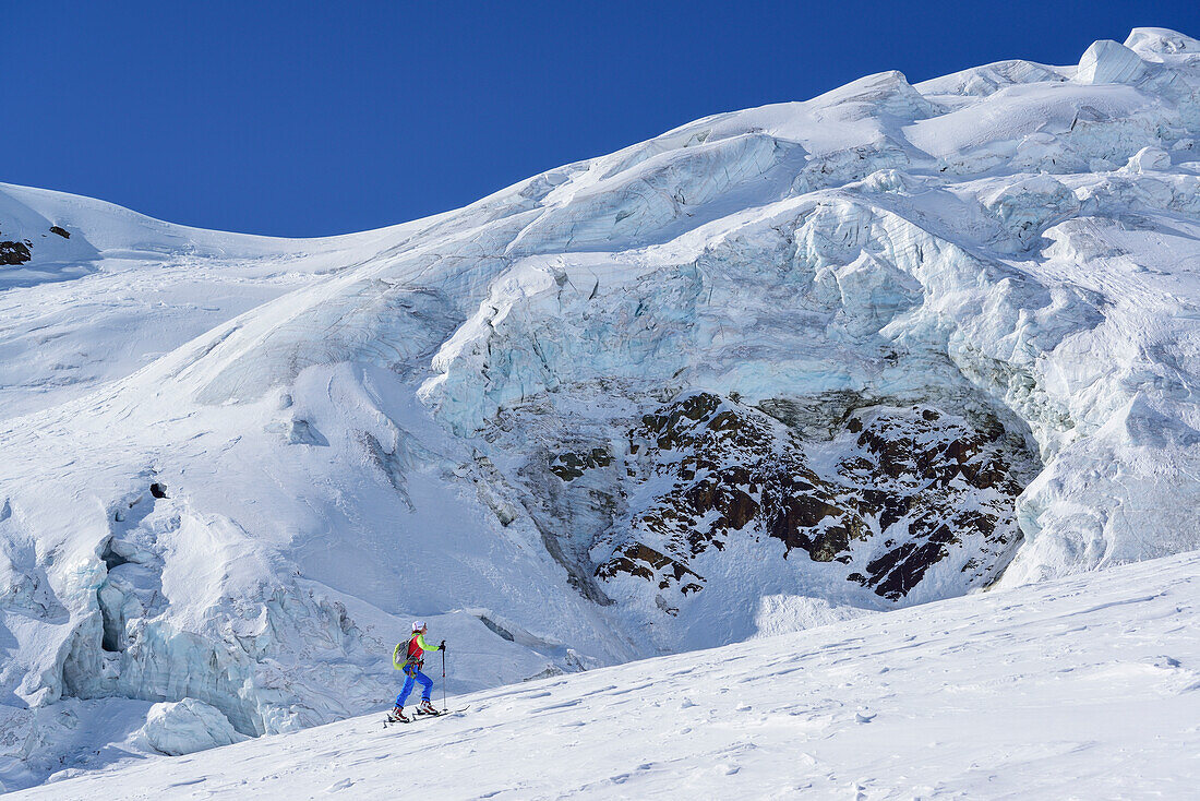 Woman back-country skiing ascending towards icefall, Punta San Matteo, Val dei Forni, Ortler range, Lombardy, Italy