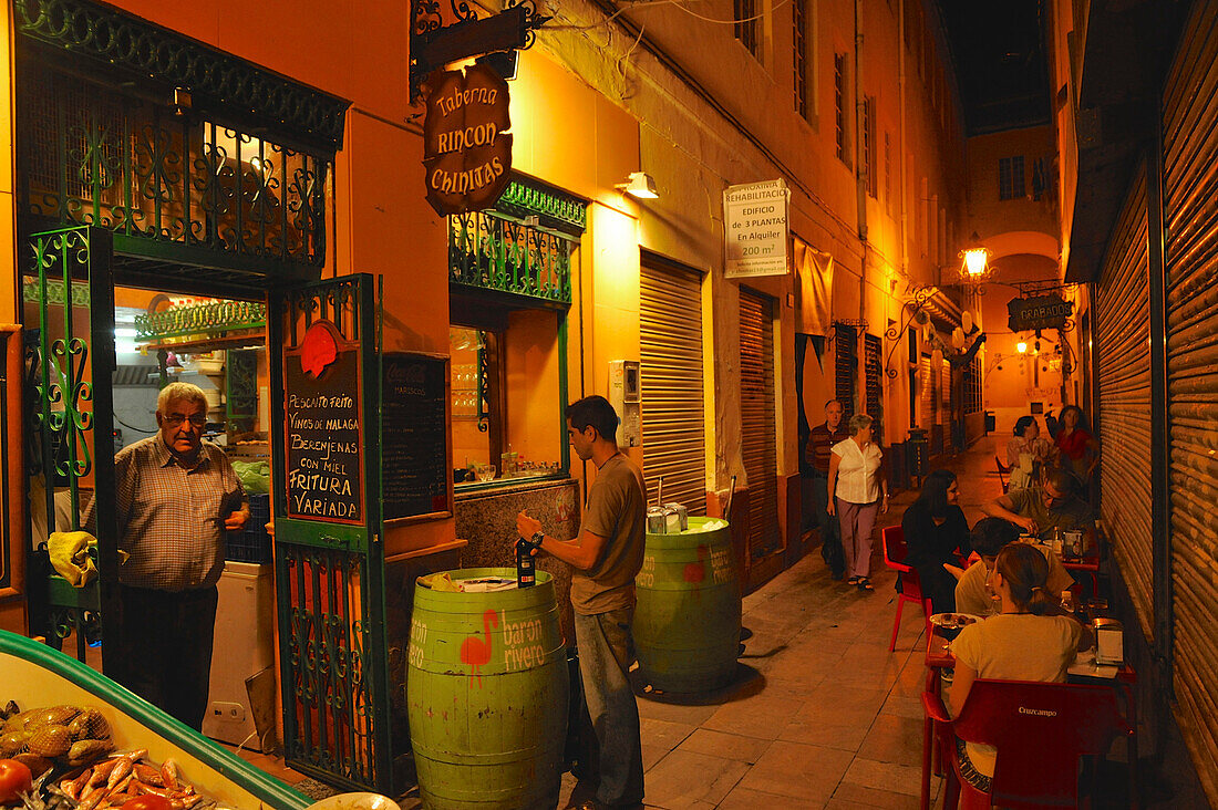 Schmale Gasse mit Tischen und Restaurant mit Meeresfrüchten nahe der Kathedrale von von Malaga im Abendlicht, Malaga, Andalusien, Spanien