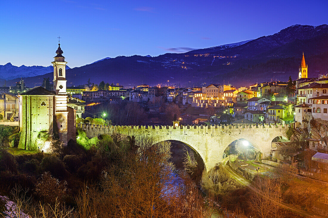 Illuminated village of Dronero with Ponte del Diavolo and river Maira, Dronero, Valle Maira, Cottian Alps, Piedmont, Italy