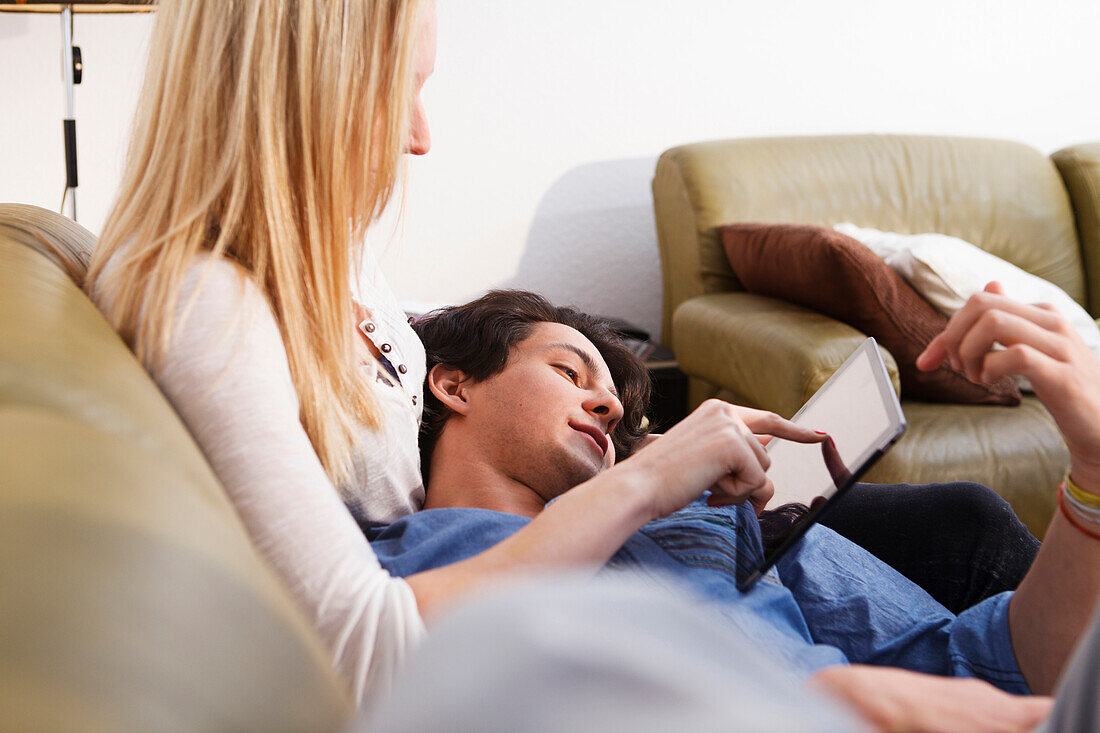 Junges Paar zuhause, kuscheln auf dem Sofa, spielt auf dem Tablet