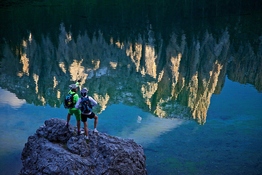 two mountain bikers at lake Karersee with reflection of Latemar, Trentino Italy