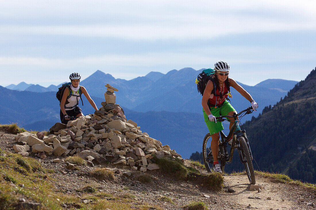 two mountain bikers on a single-trail with a cairn, Trentino Italy