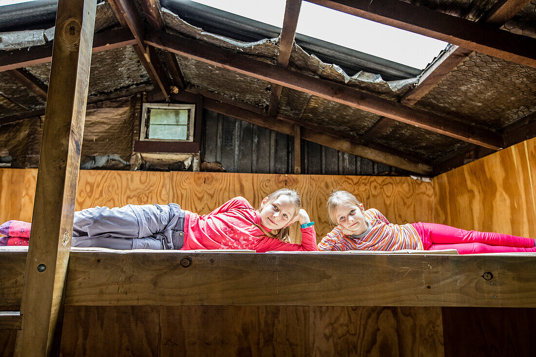 Zwei Mädchen auf dem Bett einer Hütte, Tramping Fjordland, Lake Manapouri, Südinsel, Neuseeland