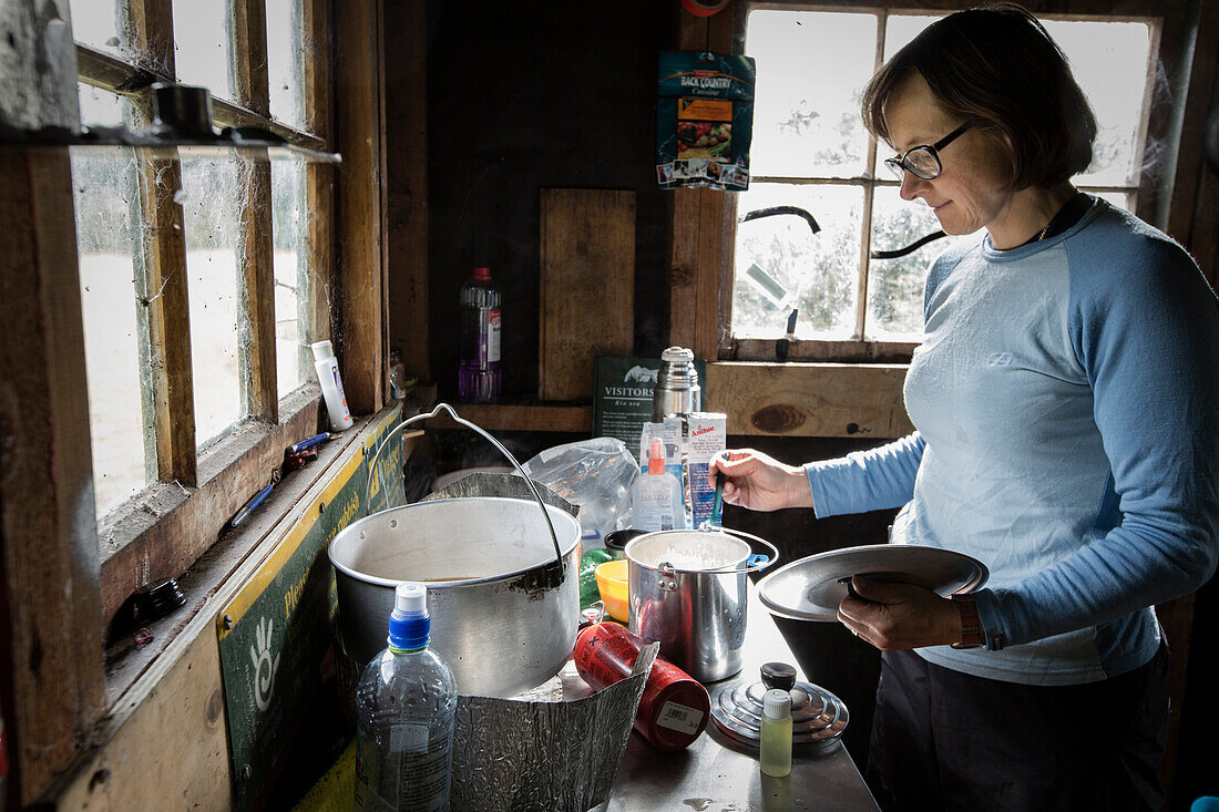 A women cooking in the shabby Back Water Hut (DOC), Fjordland, Lake Manapouri, South Island, New Zealand