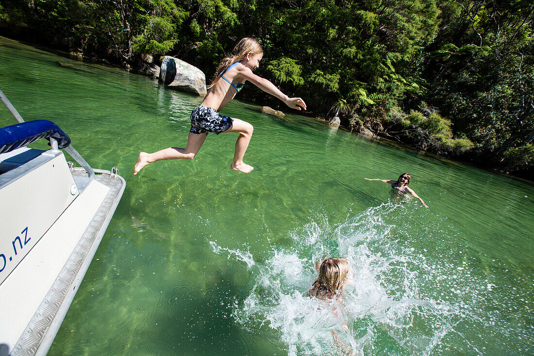 Zwei Mädchen springen ins Wasser, Motorboot in der Bucht Falls Creek. Abel Tasman Nationalpark, Südinsel, Neuseeland