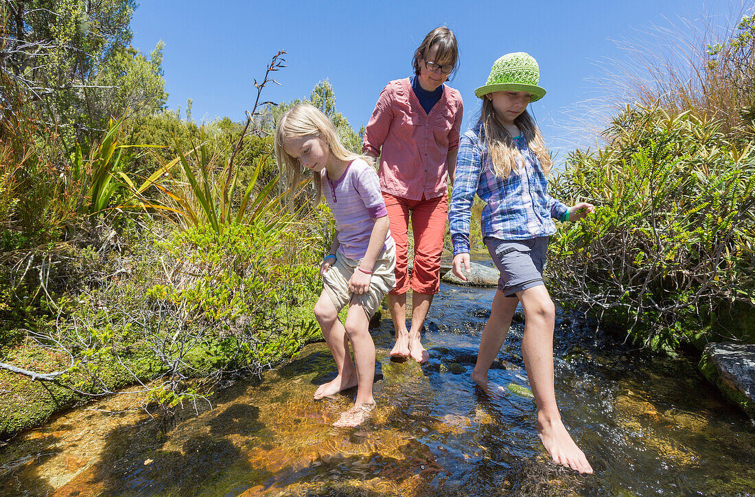 Zwei Mädchen und eine Frau waten barfuss in einem Bach, Abel Tasman Nationalpark, Südinsel, Neuseeland