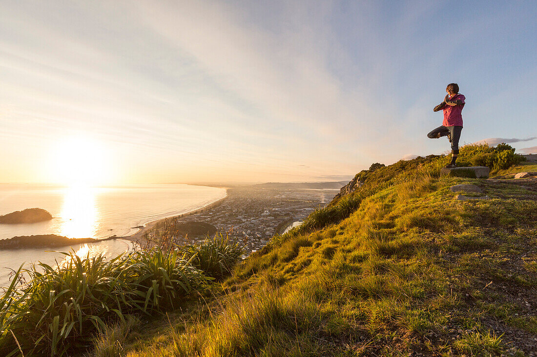 Eine Frau macht Yoga bei Sonnenaufgang auf dem Mount Maunganui, Nordinsel, Neuseeland
