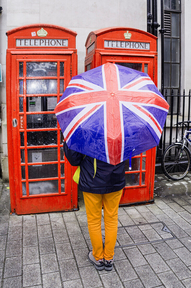 Frau mit Regenschirm vor ropten Telefonzellen, London, UK