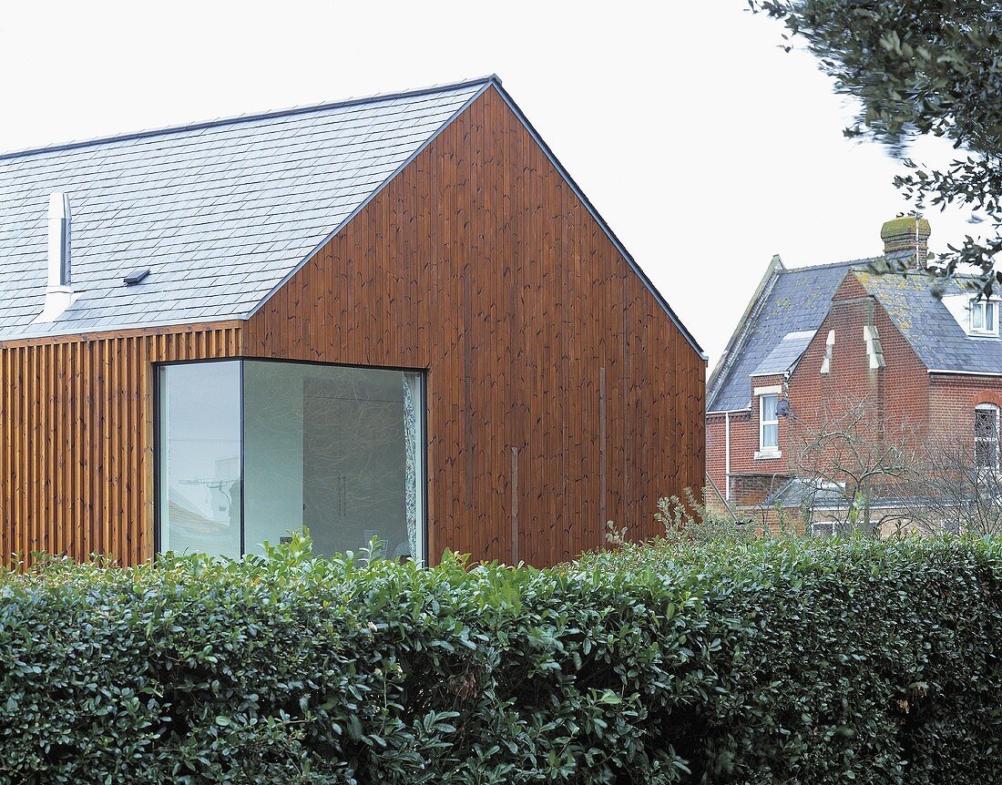 Vertical wood panelling on a newly built house with a corner window and a hedge