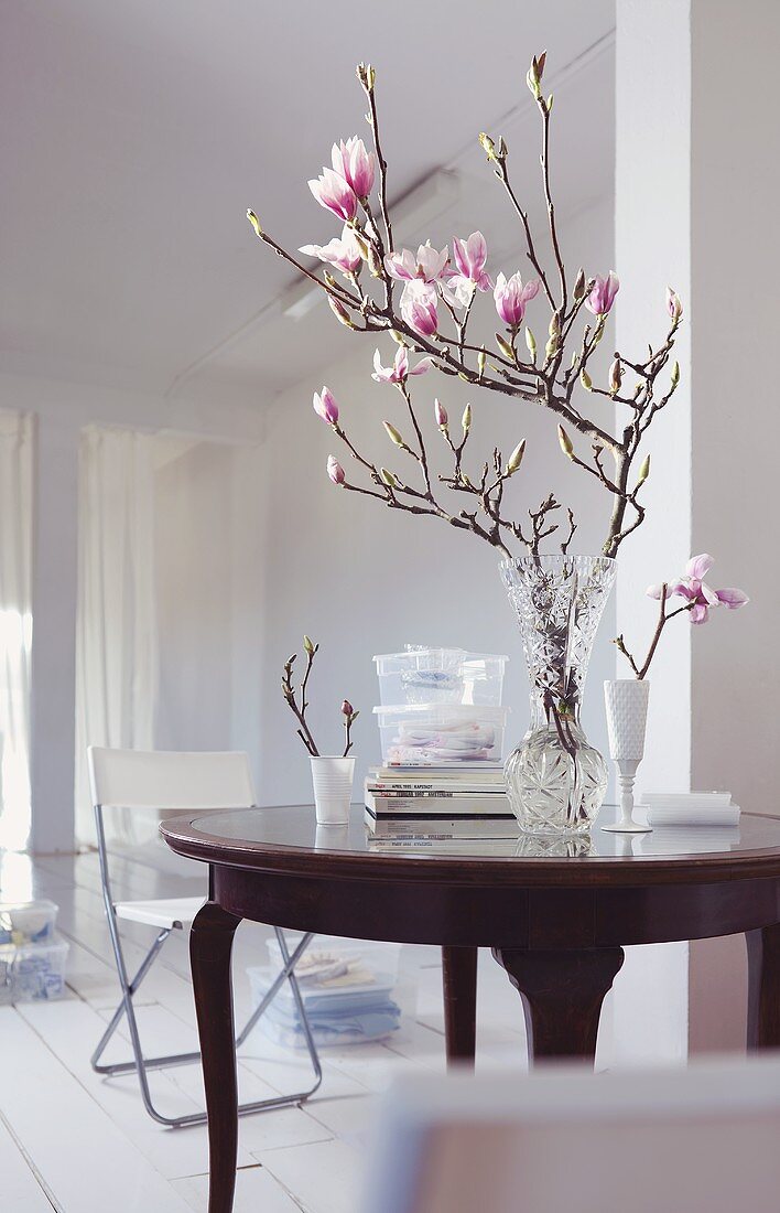 A magnolia sprig in a glass vase on an antique table in a white room