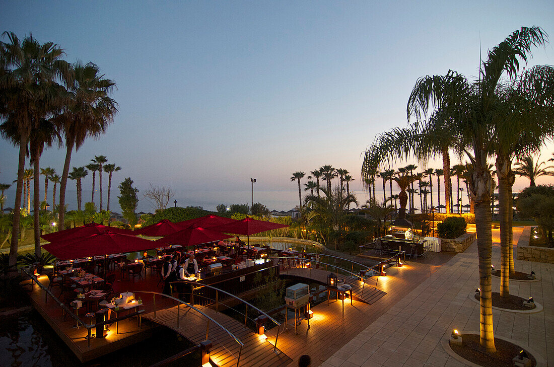 Garden restaurant with palm trees and sea after sunset in the Le Meridien Hotel, Limassol, Limassol District, Cyprus