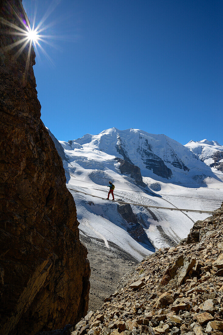 Woman on a suspension bridge climbing the via ferrata at Piz Trovat with view to Piz Palue (3905 m), Bellavista (3922 m) and Pers glacier, Engadin, Grisons, Switzerland