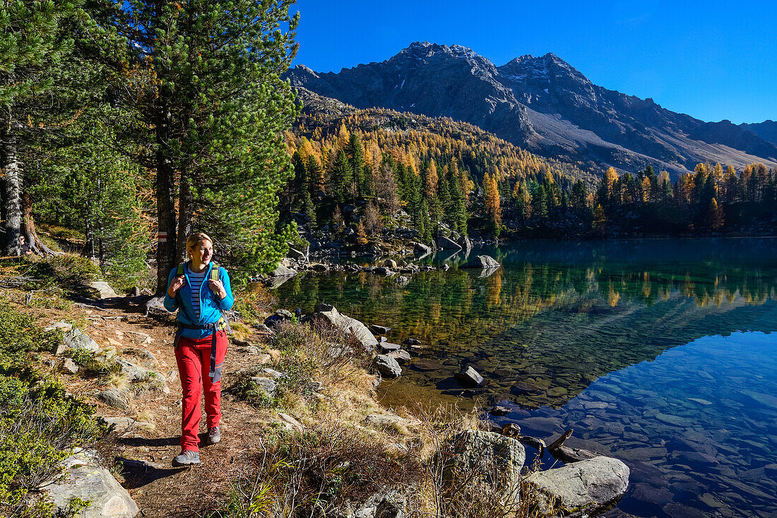 Woman hiking along the shore of lake Saoseo (2028 m) with Cima da Rugiul (2987 m) and Piz dal Teo (3049 m), Valposchiavo, Grisons, Switzerland