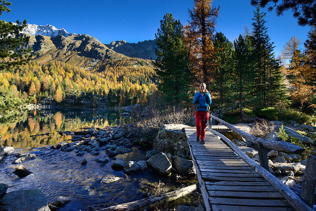 Woman hiking over a river on a bridge at the shore of lake Saoseo (2028 m) with Scima di Saoseo (3264 m), Valposchiavo, Grisons, Switzerland