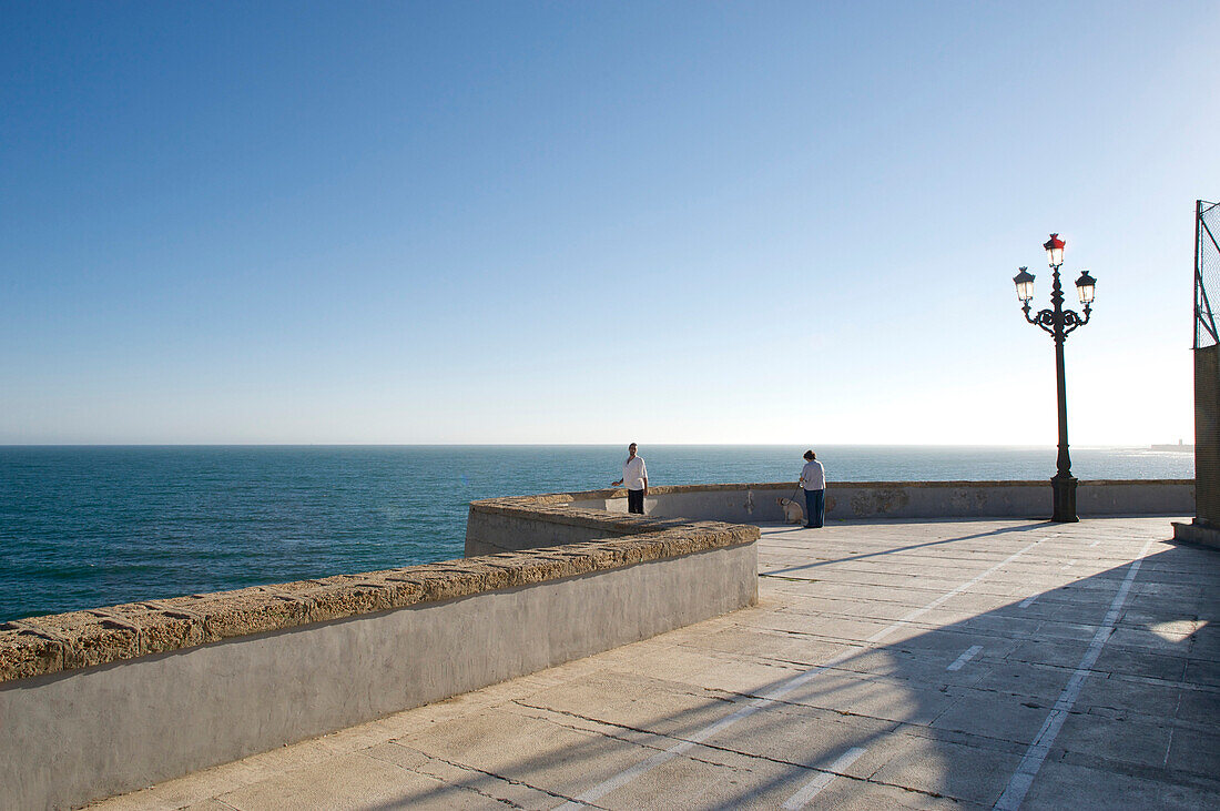 Promenade by the sea with wall and old style electric light, view across the sea with two lonesome people, Cadiz, Andalusia, Spain, Europe