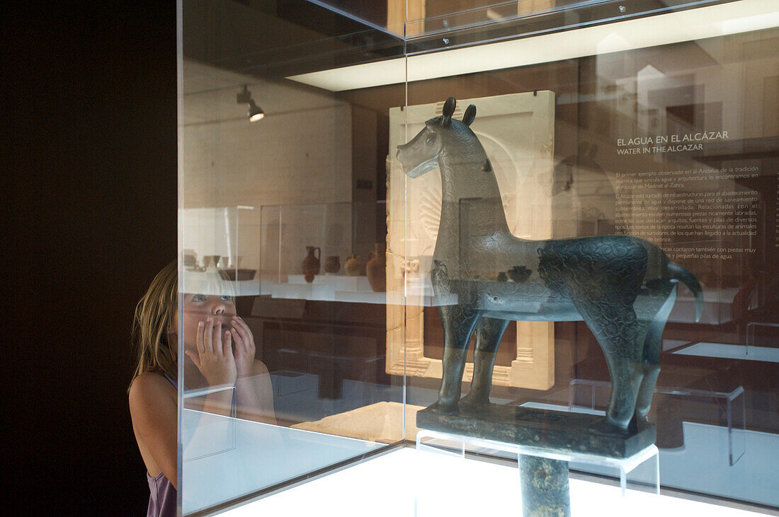 Girl astonished by a bronze sculpture of a horse in the visitors center at Medina Azahara, Cordoba, Andalusia, Spain