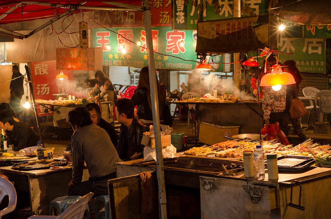 Leute essen an den Essensständen auf dem Nachtmarkt der Stadt Kaili, Provinz Guizhou, China