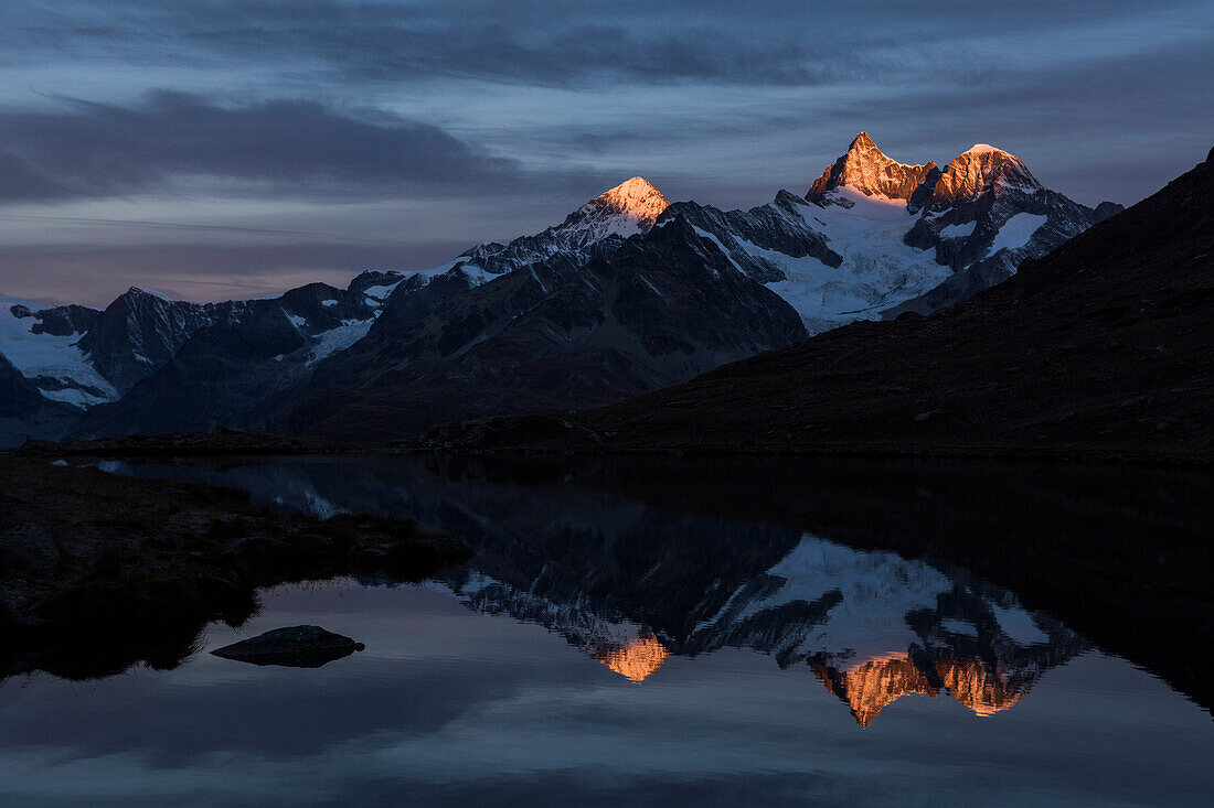Dent Blanche, Ober Gabelhorn und Wellenkuppe, von links nach rechts, spiegeln sich kurz nach Sonnenaufgang im Stellisee, Walliser Alpen, Kanton Wallis, Schweiz