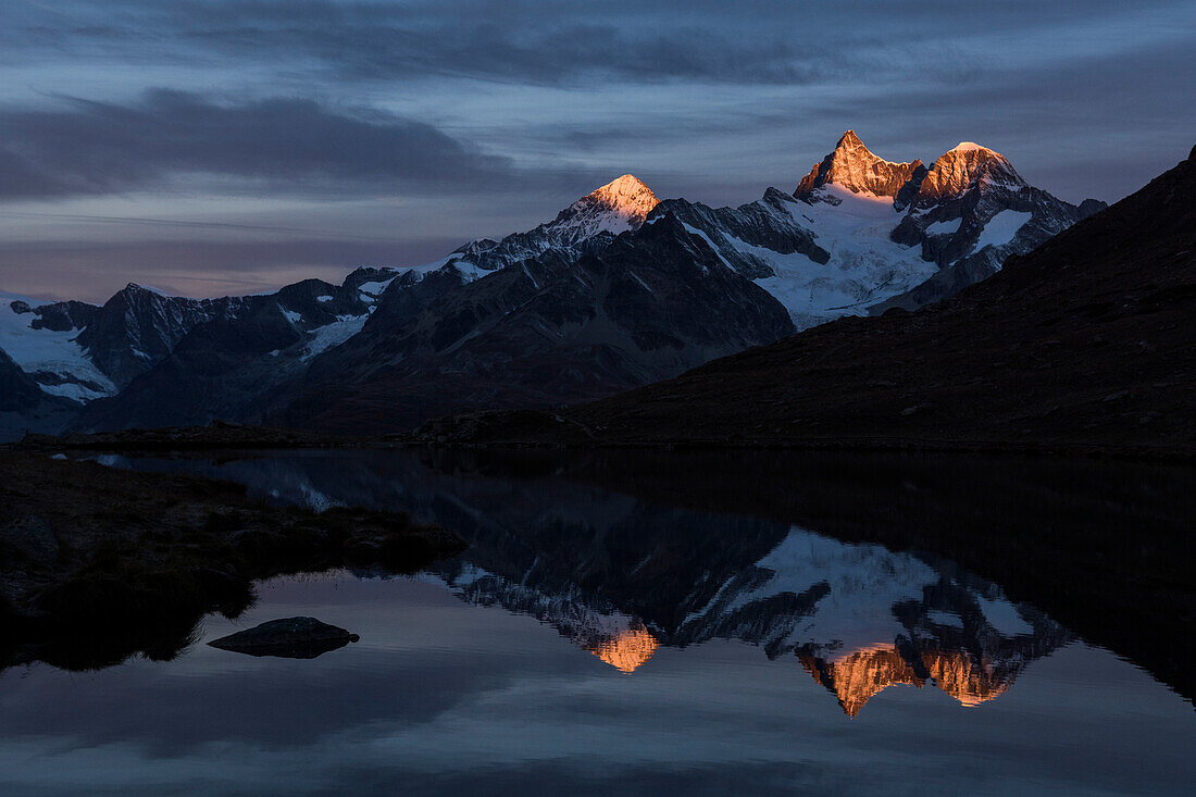 Lake Stelli reflecting the summits of Dent Blanche, Ober Gabelhorn and Wellenkuppe, from left to right, just after sunrise, Pennine Alps, canton of Valais, Switzerland