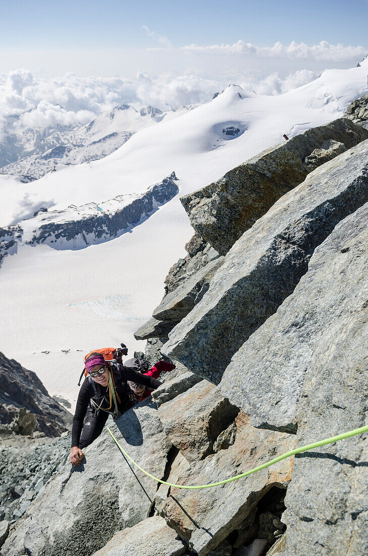 A young woman in mountaineering gear climbing a rock passage, Hohlaub Ridge, Allalinhorn, Pennine Alps, canton of Valais, Switzerland