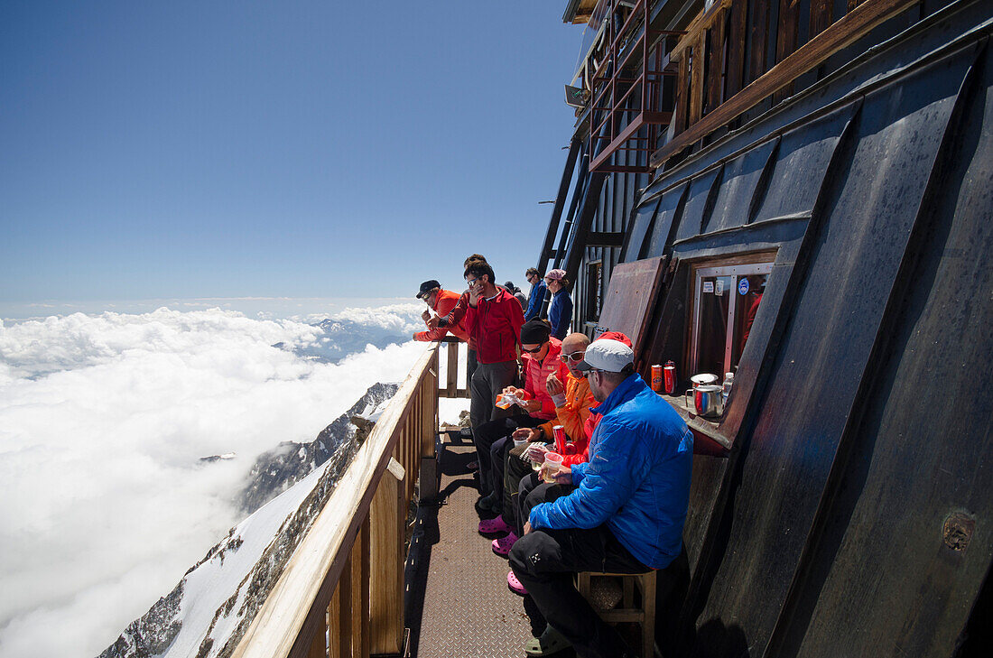 Bergsteiger vor der Margherita Hütte auf dem Gipfel der 4554 Meter hohen Signalkuppe oder Punta Gnifetti, höchste Hütte der Alpen, drunter das Wolkenmeer über Norditalien, Monte Rosa Massiv, Walliser Alpen, Italien