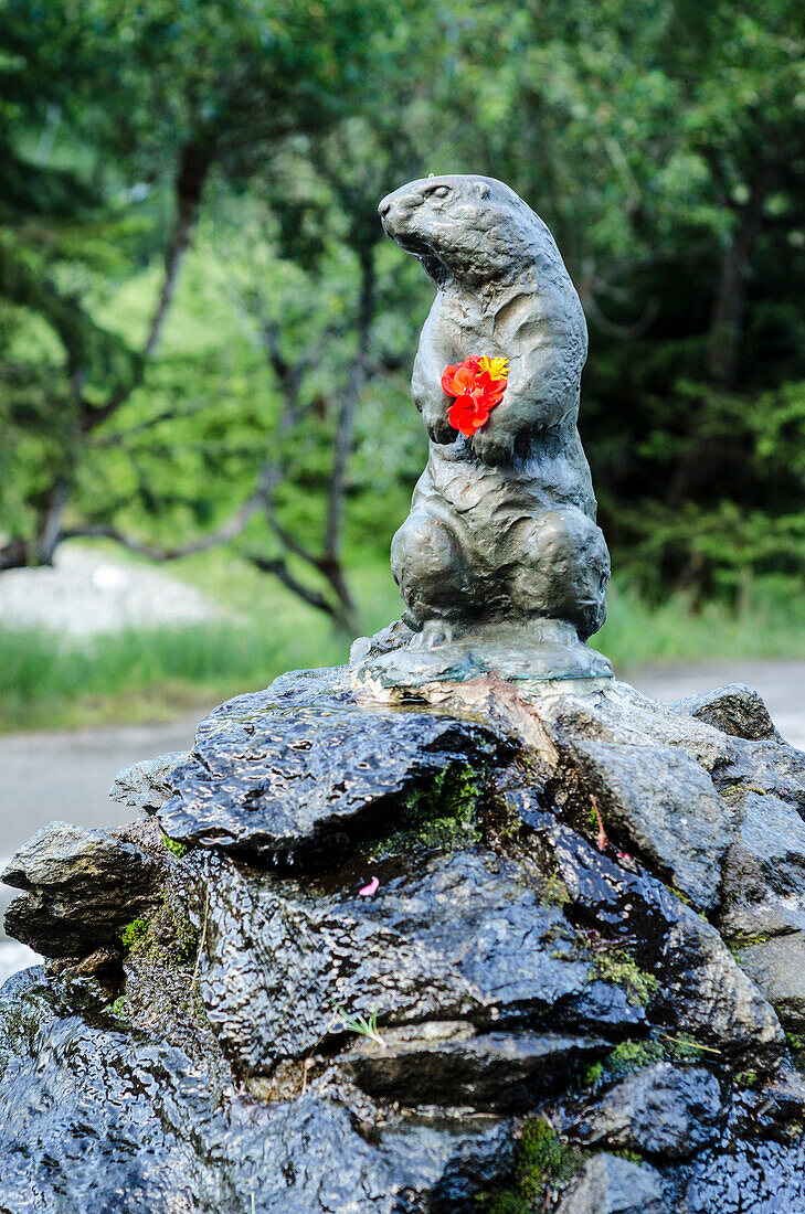 A bronze marmot with fresh flowers in its paws on a fountain, Champex, canton of Valais, Switzerland