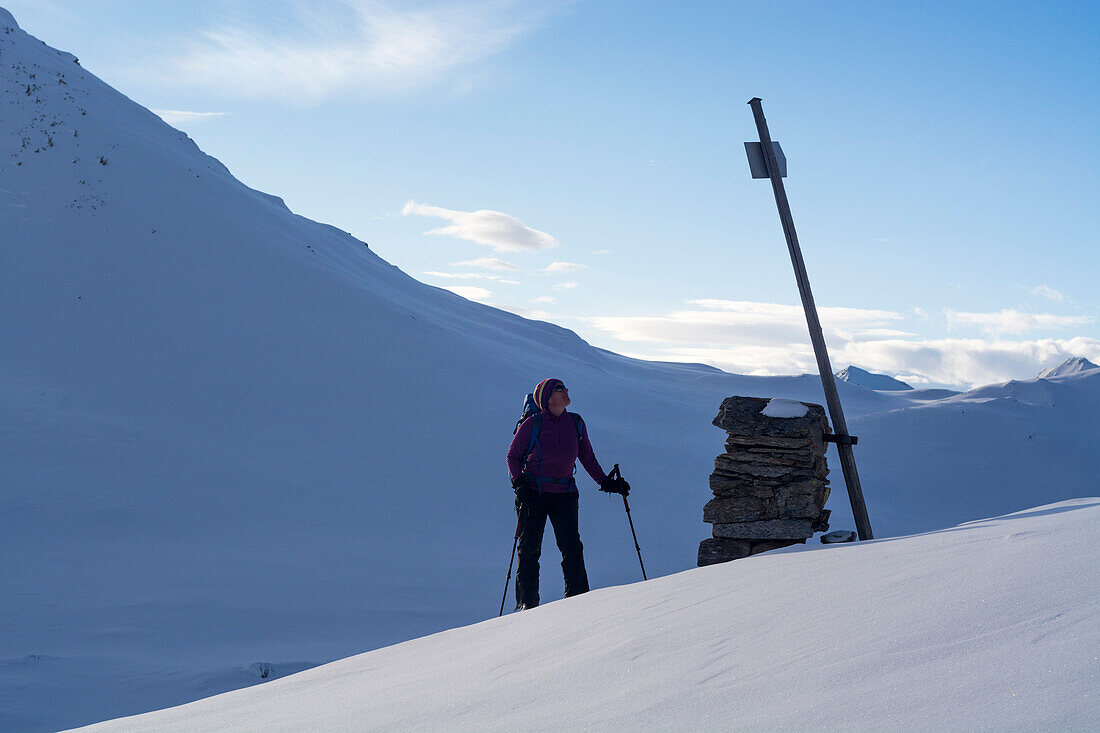 A female backcountry skier looking at a signpost in the snowy valley called Val Camadra, Lepontine Alps, canton of Ticino, Switzerland