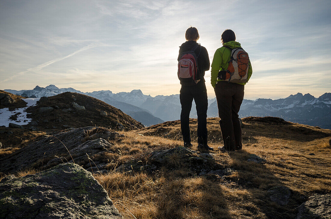 Two women in hiking gear standing on an alpine meadow near the alp of Fessis and looking towards the summits of the Glarus Alps, canton of Glarus, Switzerland