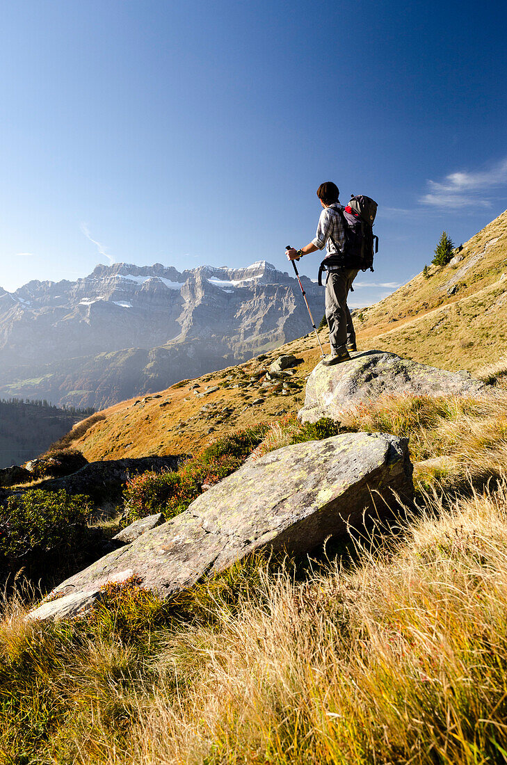 A young hiker standing on a rock near the alp of Mettmen and looking towards the summits of the Glaernisch massif, Glarus Alps, canton of Glarus, Switzerland