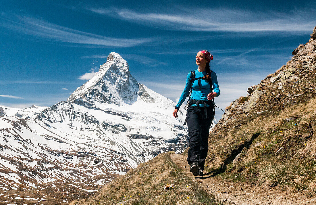 Jüngere Frau wandert auf schmalem Weg mit Blick auf Matterhorn, Walliser Alpen, Wallis, Schweiz