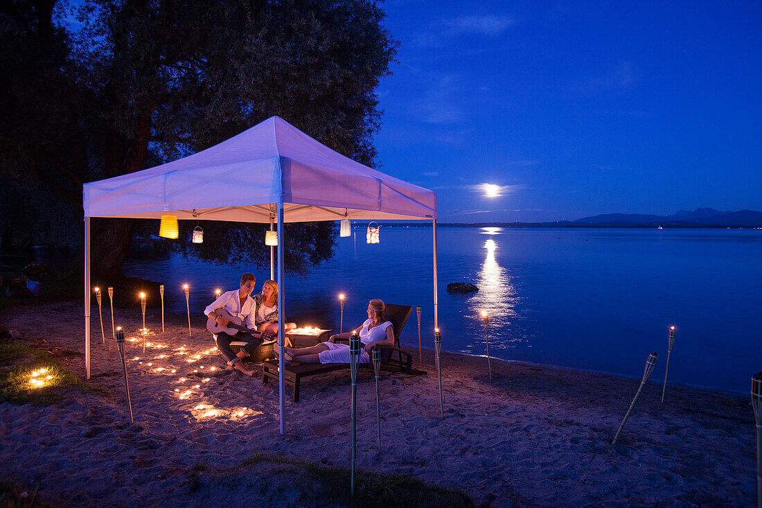 Young people sat under a tent with lampions in full moon, Krautinsel, Chiemsee, Bavaria, Germany