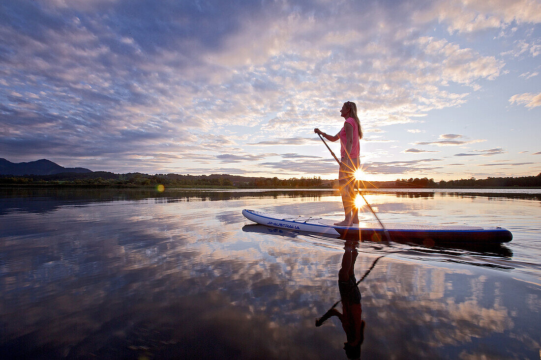 Woman stand up paddling on lake Chiemsee in sunset, Chiemgau, Bavaria, Germany