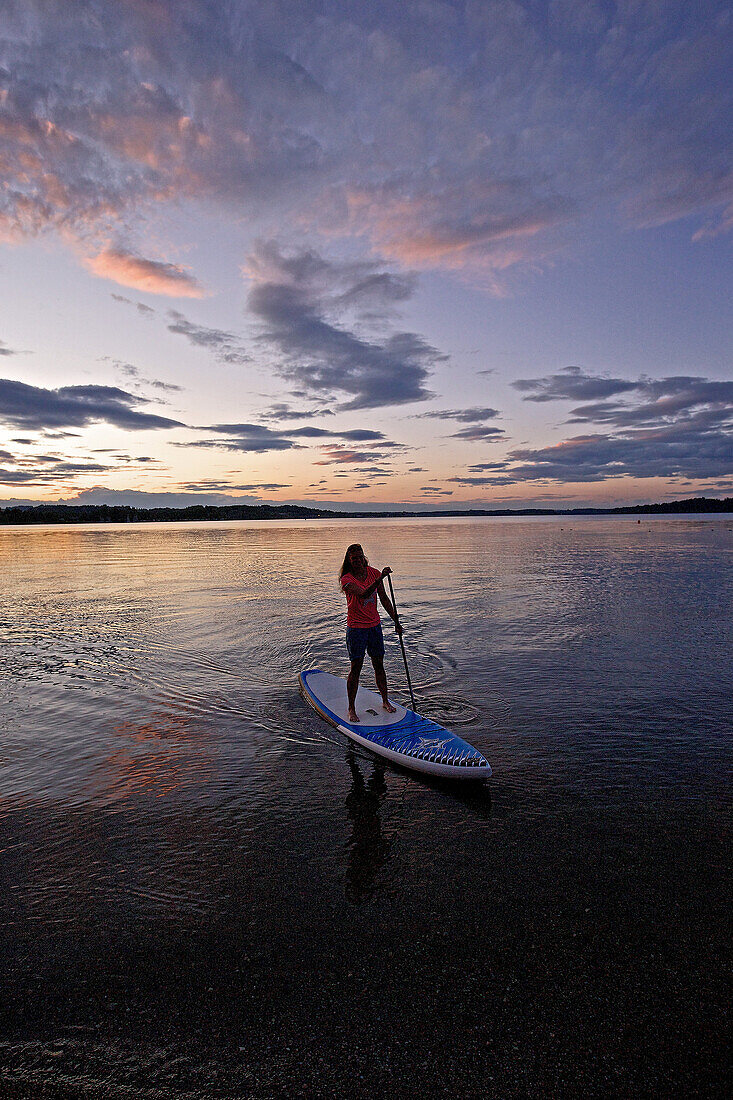 Frau beim Stand Up Paddling auf dem Chiemsee im Sonnenuntergangs, Chiemgau, Bayern, Deutschland