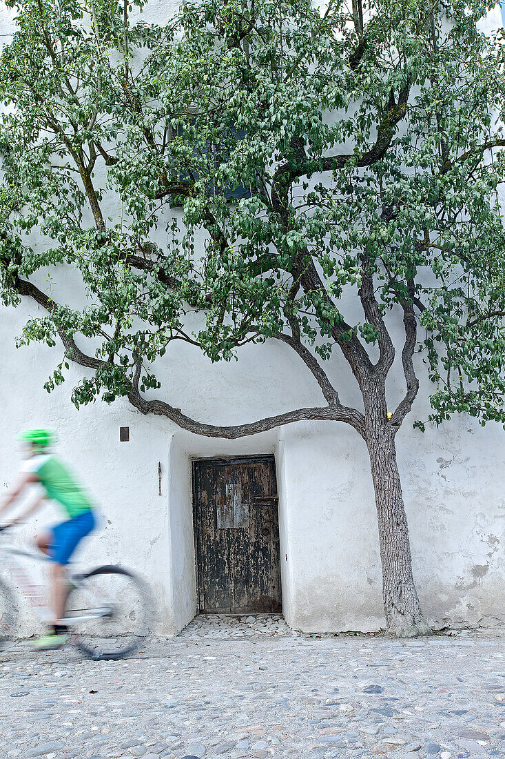 Fahrradfahrerin fährt an einer alten Tür zum Folterturm der Burg vorbei, Burghausen, Chiemgau, Bayern, Deutschland