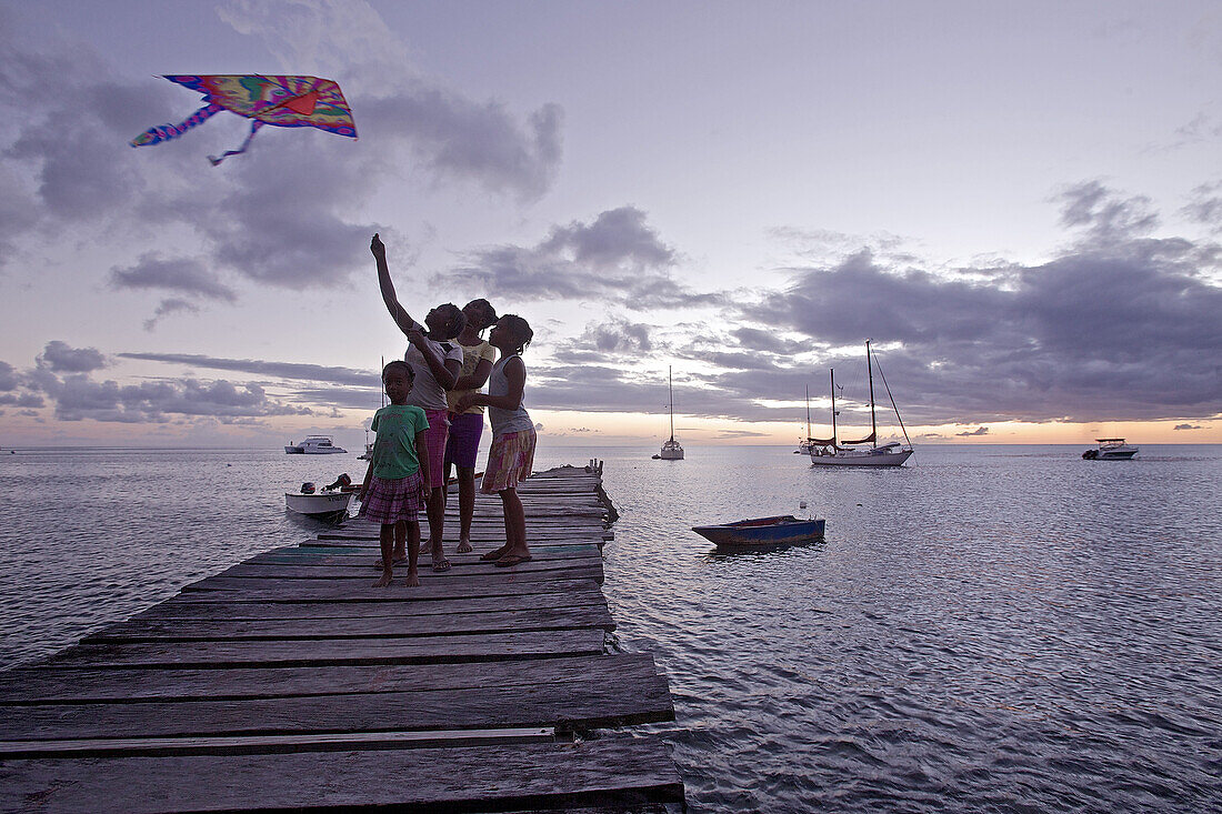 Kinder spielen auf einem Steg mit einem Drachen im Sonnenuntergang, Dominica, Kleine Antillen, Karibik