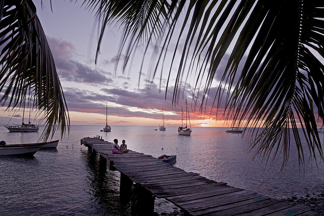 Kinder sitzen auf einem Holzsteg am Meer im Sonnenuntergang, Dominica, Kleine Antillen, Karibik