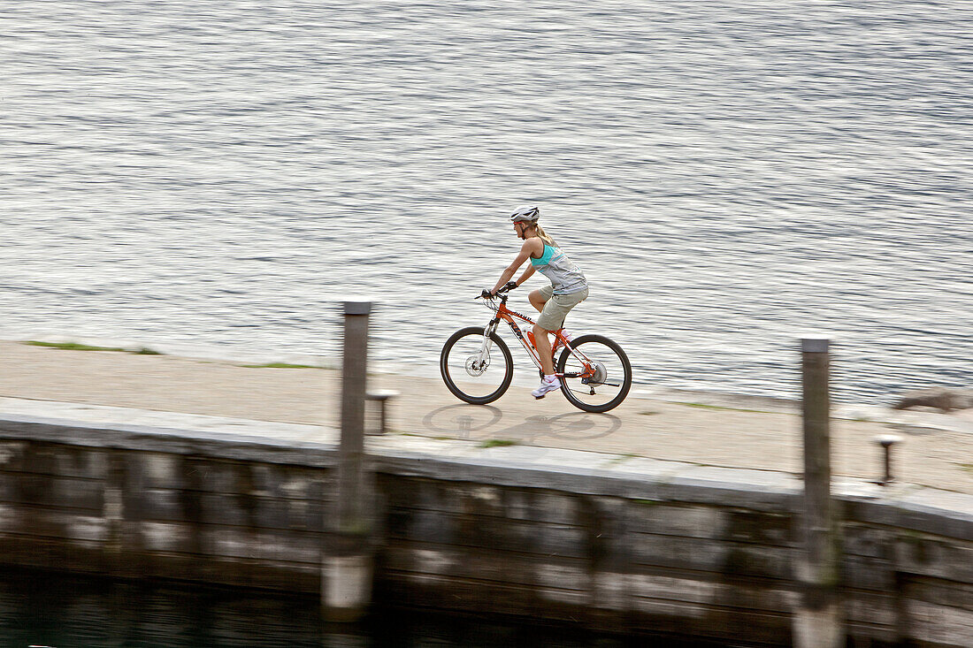 Junge Frau fährt mit ihren Fahrrad am Hafen an einem See, Gardasee, Italien