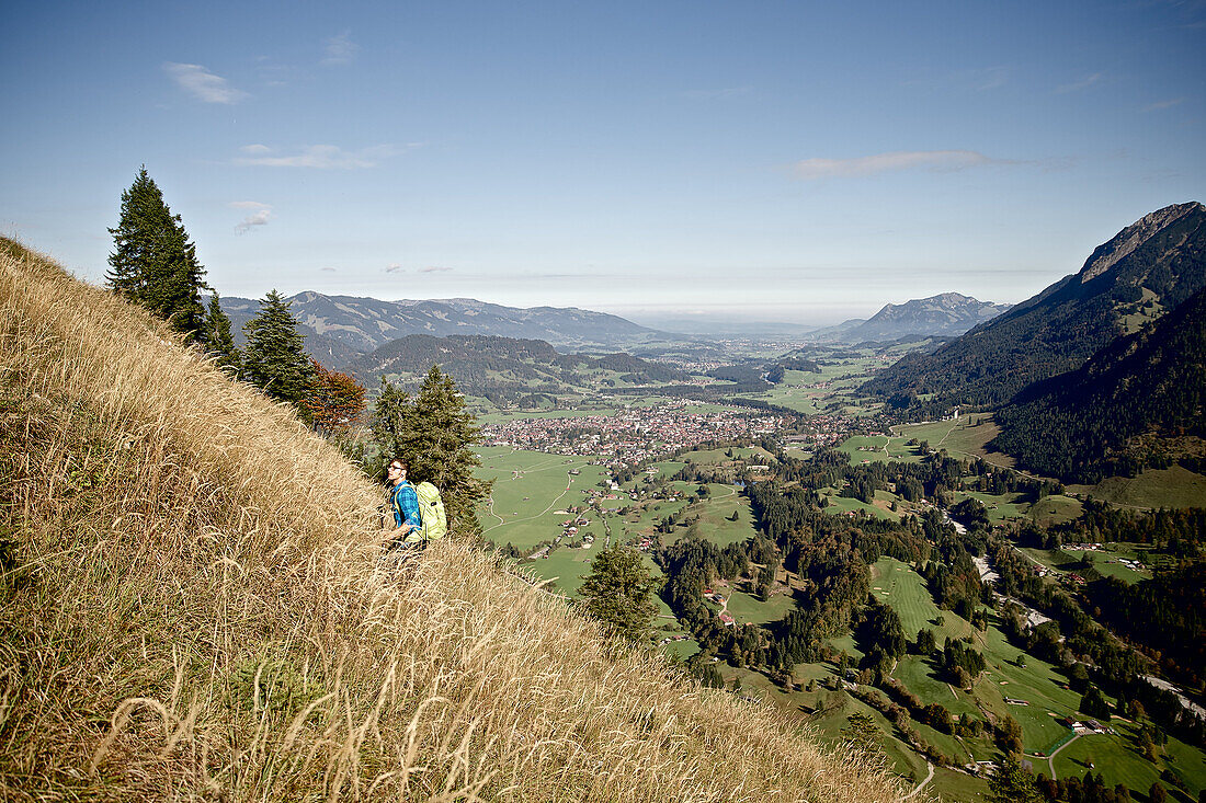 Junger Mann wandert einen Berg hinauf an einem sonnigen Tag, Oberstdorf, Bayern, Deutschland
