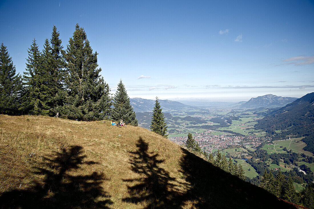 Zwei junge Wanderer machen eine Pause mit Blick auf ein Dorf, Oberstdorf, Bayern, Deutschland