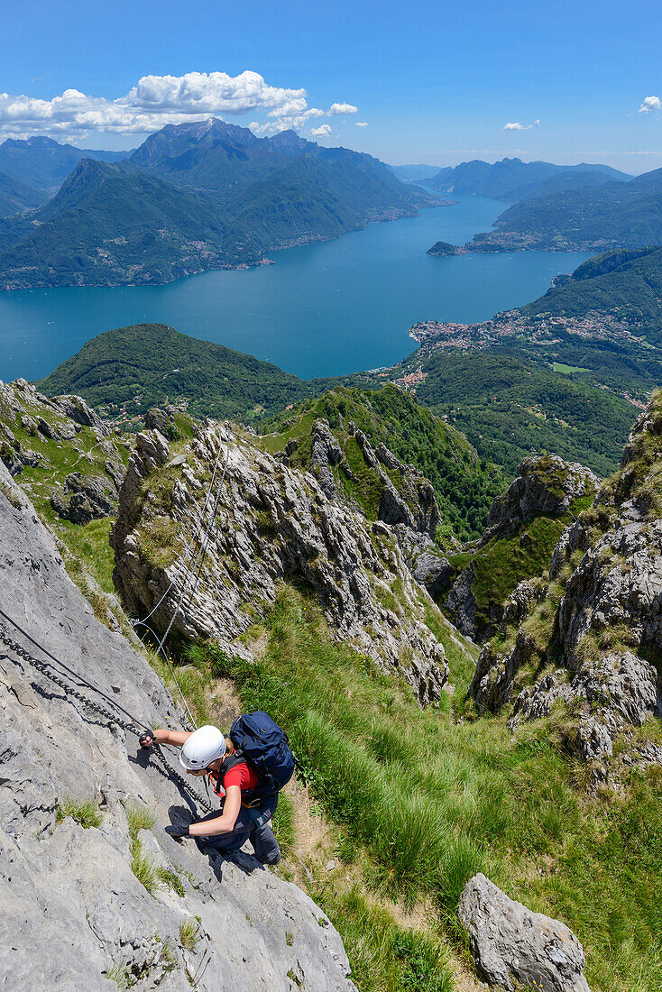 Woman climbing the Via ferrata del Centenario in front of Menaggio on the right-hand shore of Lake Como and Grigna Settentrionale (2408 m) above it, Lombardei, Italy