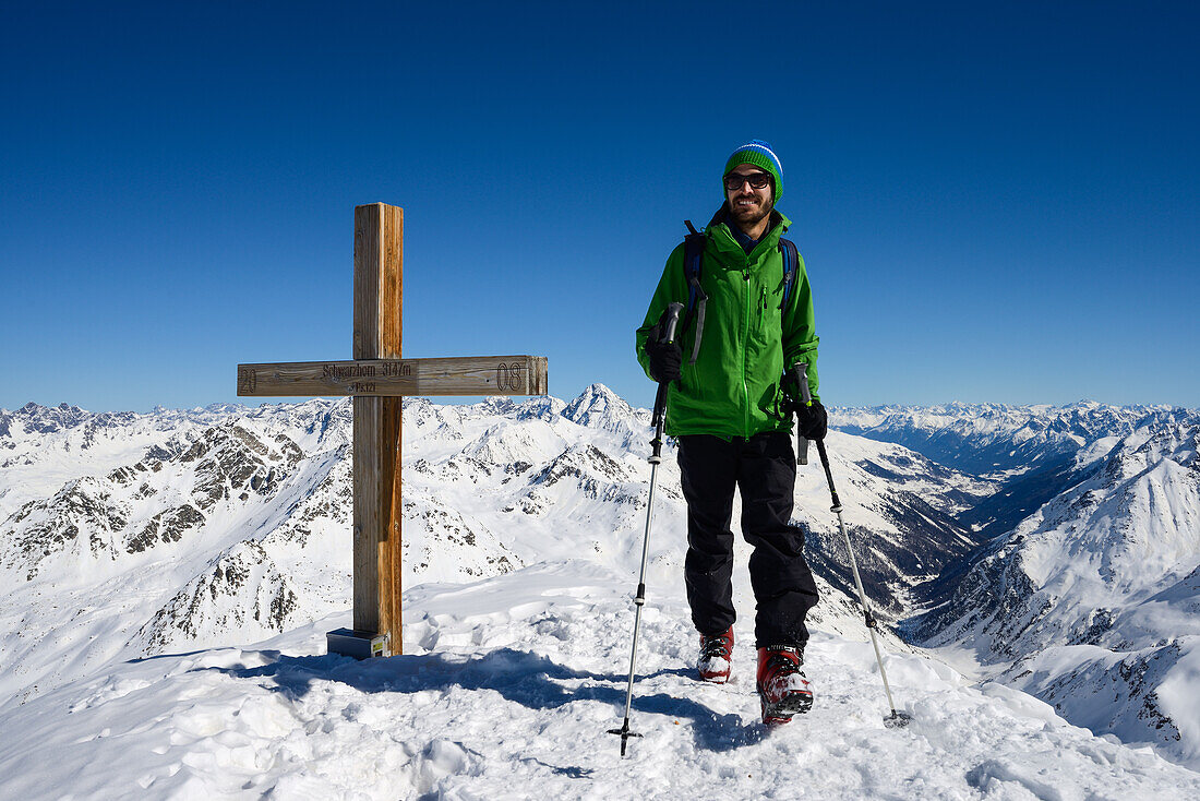 Man at the summit cross of the Schwarzhorn (3147 m), in the middle of the picture Piz Linard (3410 m), Grisons, Switzerland, Europe